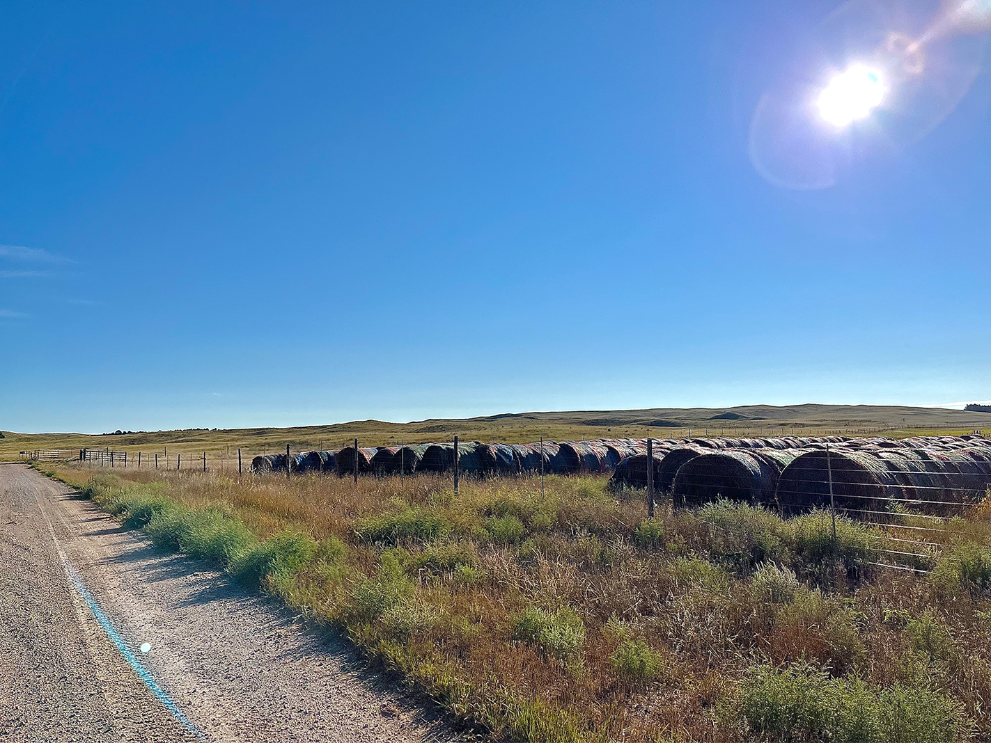Hay bales line the side of a gravel road. 